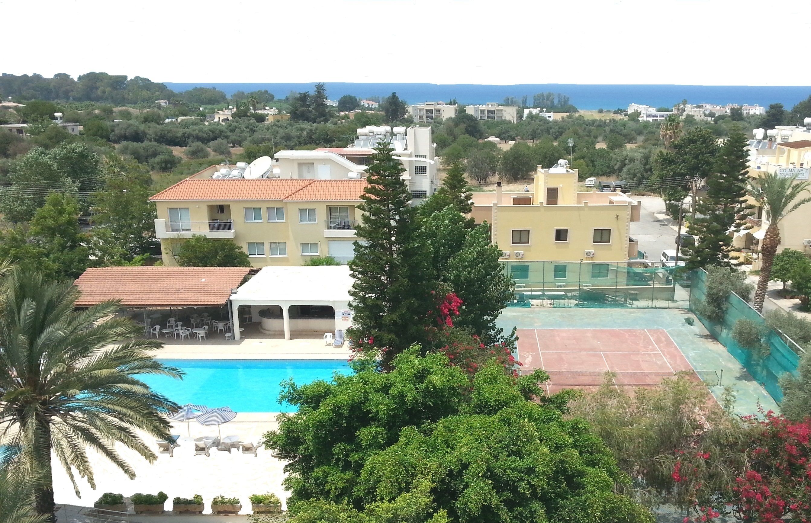 A residential area with a swimming pool, tennis court, and a view of the sea.