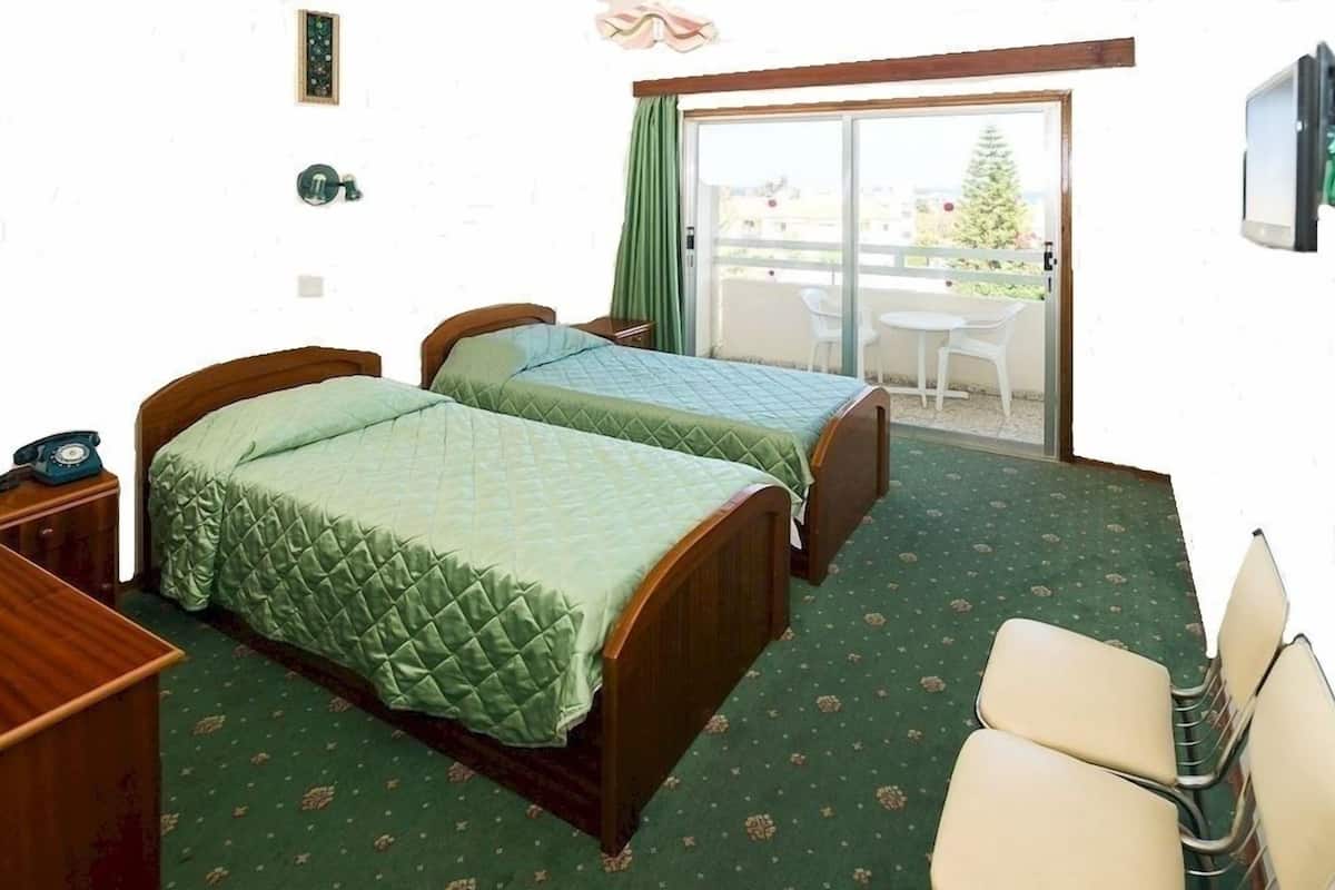 A hotel room with two beds, a desk, a chair, and a balcony with a view of a Christmas tree.