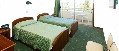 A hotel room with two beds, a desk, a chair, and a balcony with a view of a Christmas tree.