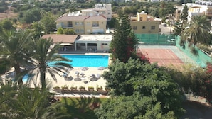 A residential area with a swimming pool, palm trees, and a tennis court. - Marion (Polis)