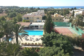 A residential area with a swimming pool, palm trees, and a tennis court.