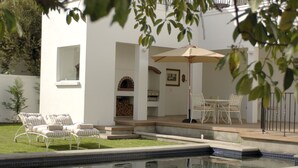 A poolside area with lounge chairs, a table, and an umbrella. - Beauclair Guest Cottage (Stellenbosch)