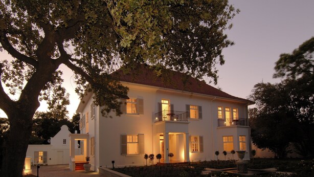 A two-story white building with a balcony, a covered entrance, and a landscaped garden. - Beauclair Guest Cottage (Stellenbosch)