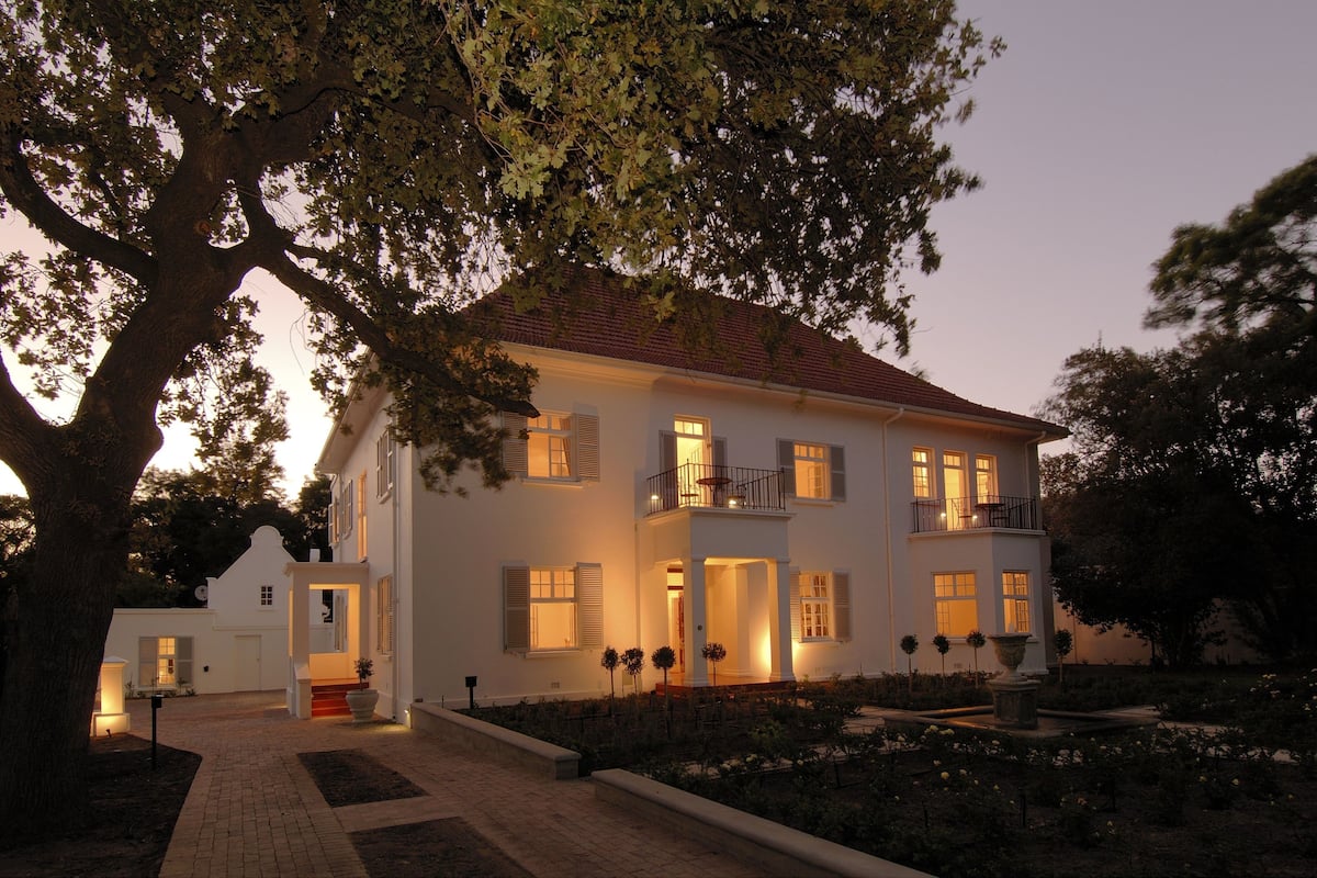 A two-story white building with a balcony, a covered entrance, and a landscaped garden.