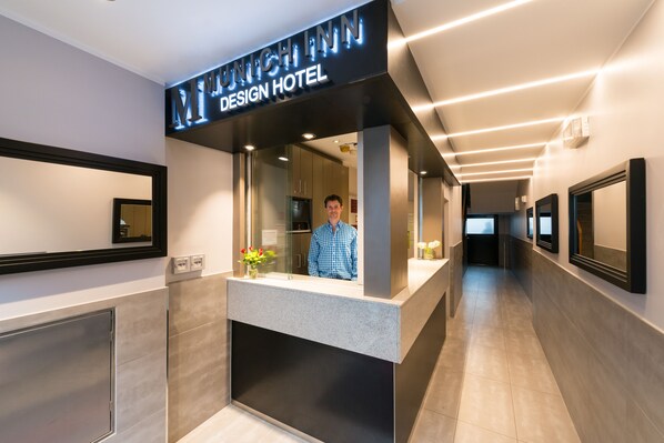A reception desk at the Munich Inn Design Hotel with a modern interior and a person standing behind it.