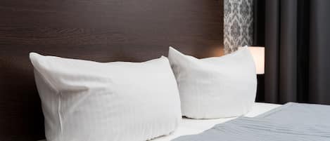 A neatly made bed with white pillows and a gray blanket, a wooden headboard, and a wall-mounted light fixture.