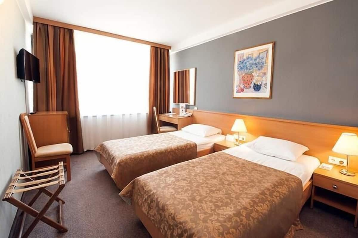 A hotel room with two beds, a desk, a chair, a TV, and a painting on the wall.