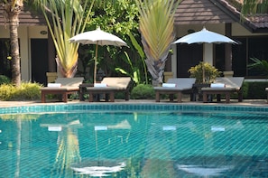 A pool area with lounge chairs and umbrellas, surrounded by tropical plants and a building with a tiled roof. - Laluna Hotel & Resort (Chiang Rai)
