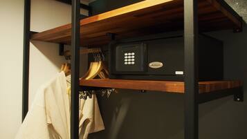 A storage compartment with a black safe, wooden shelves, and hanging clothes.