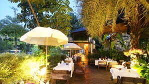 An outdoor restaurant with wooden tables and chairs, surrounded by lush greenery and decorative lighting. - Laluna Hotel & Resort (Chiang Rai)