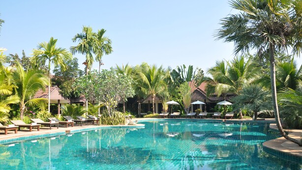 A clear blue swimming pool surrounded by lounge chairs and palm trees. - Laluna Hotel & Resort (Chiang Rai)