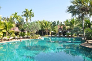 Una piscina azul cristalina rodeada de sillas de descanso y palmeras.