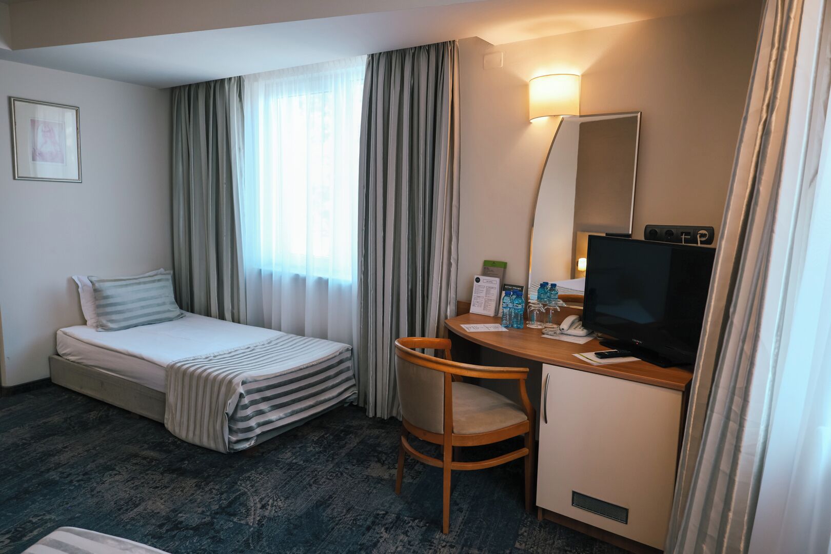 Habitación de hotel con una cama, un escritorio con ordenador, una silla y un televisor.