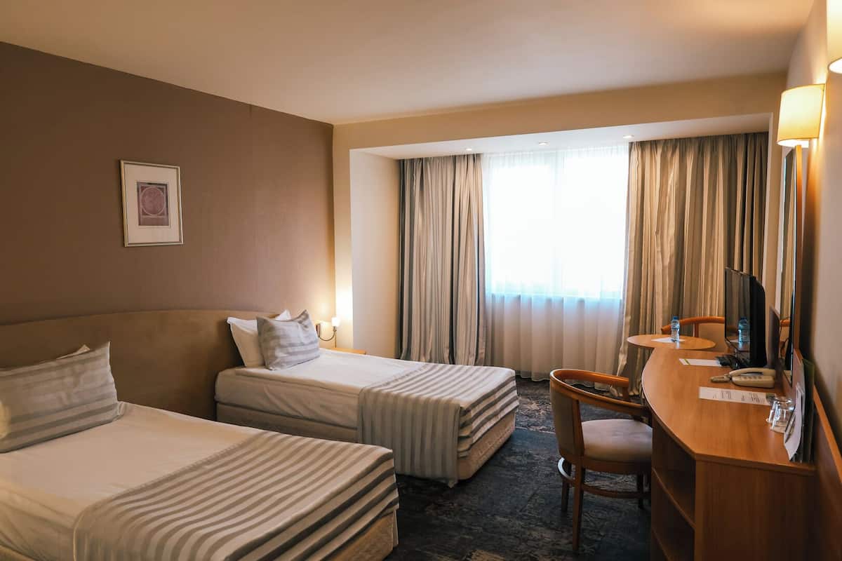 Une chambre d’hôtel avec deux lits, un bureau avec une chaise, une télévision et une fenêtre avec des rideaux.