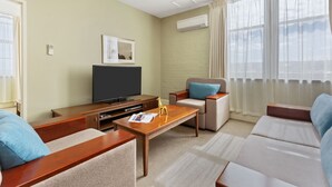 Una sala de estar moderna con un televisor de pantalla plana, una mesa de centro, sofás y un gran ventanal con cortinas.