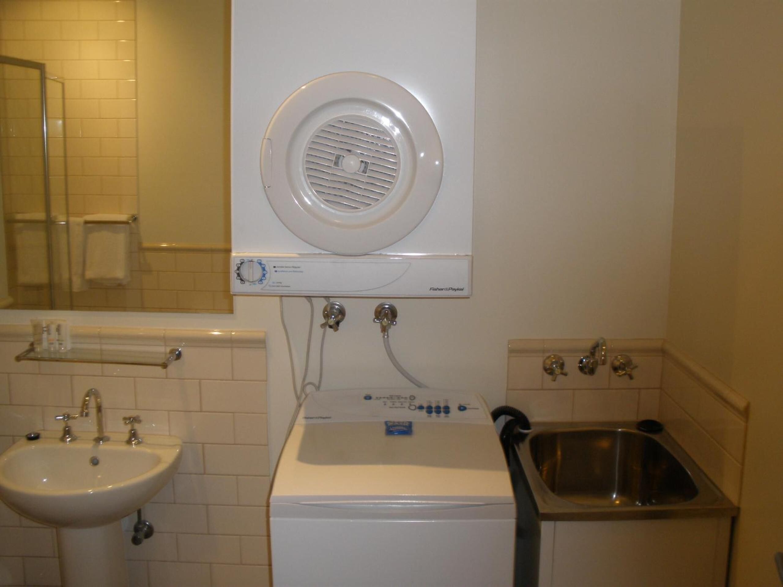 A compact bathroom with a sink, a washing machine, and a small utility sink.