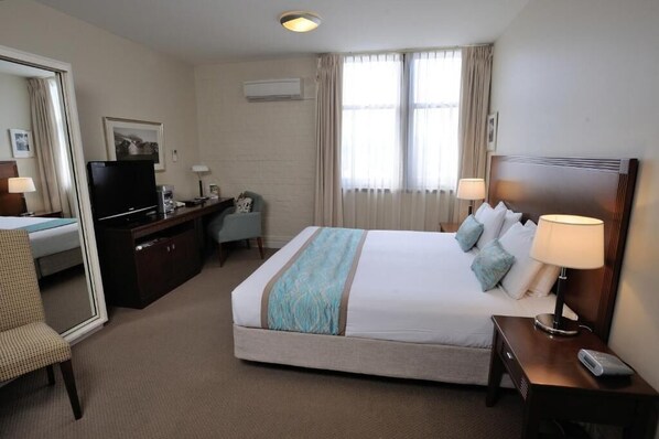A hotel room with a large bed, a desk with a television, a chair, a desk lamp, and a nightstand with a lamp. - Launceston Central Apartment Hotel (Launceston)