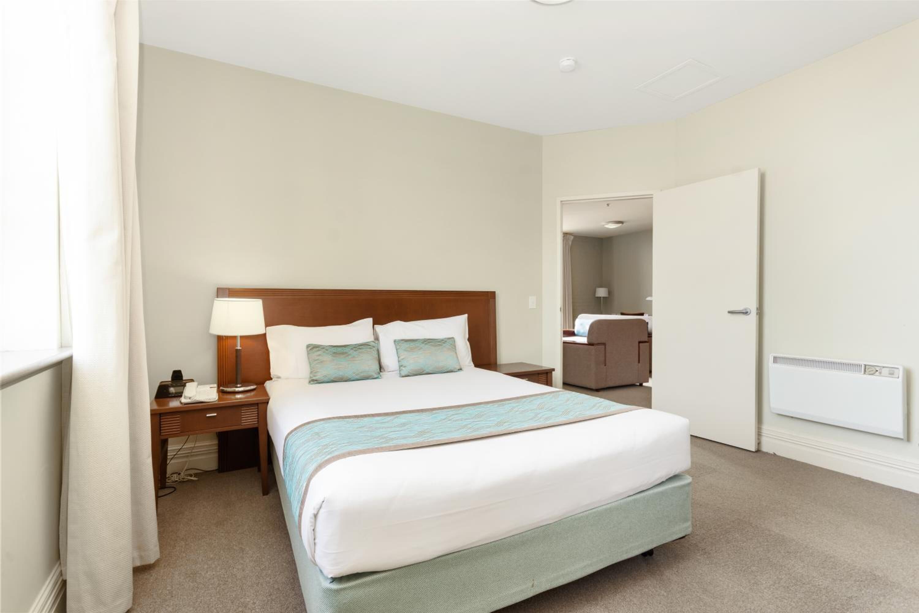 Une chambre d’hôtel avec un grand lit, des tables de chevet, une lampe, un miroir et une porte donnant sur une salle de bain.