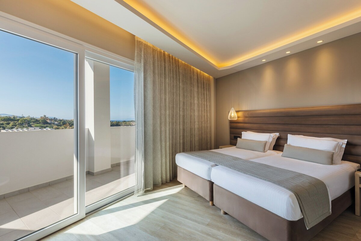 Habitació d'hotel amb un llit gran, una porta corredissa de vidre a un balcó i vista a la ciutat.