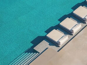 Vista aérea de una zona de piscina con agua azul cristalina y escalones con baldosas que conducen a sillones con cojines blancos.