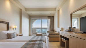 A hotel room with a large bed, a desk, a chair, a TV, and a balcony with a view.