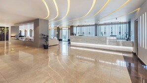 A spacious lobby with a polished marble floor, a reception desk, and a seating area with a sofa and potted plants.