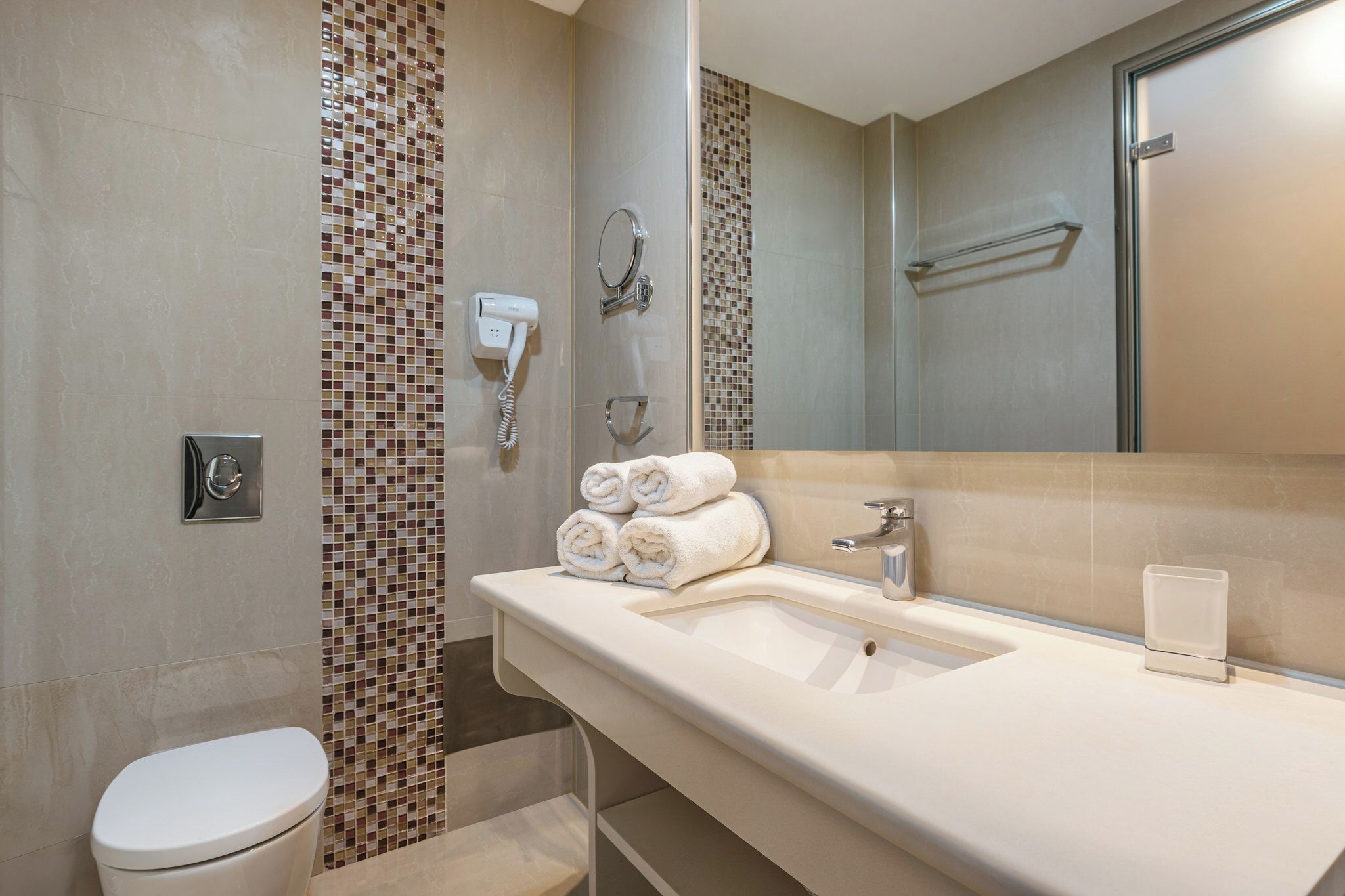A modern bathroom with a white toilet, a sink with a mirror, and a shower area with mosaic tiles.
