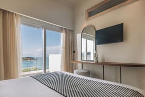 A hotel room with a large bed, a TV mounted on the wall, a window with curtains, and a view of the sea. - Alexandra Beach Resort and Spa (Zakynthos)
