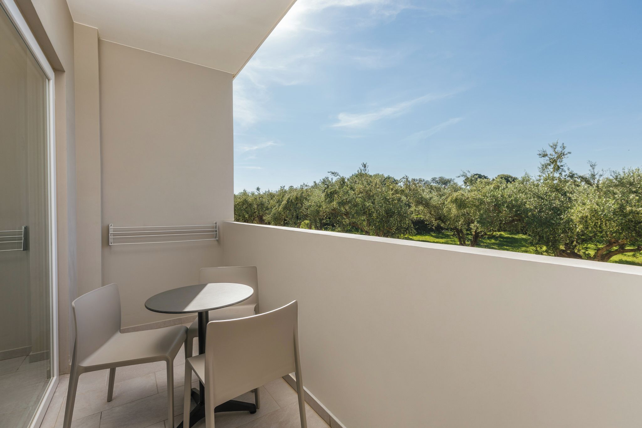 Un balcón con una mesa redonda y dos sillas, con vistas a un jardín con árboles y arbustos.