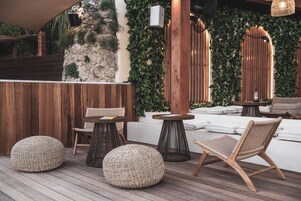 A wooden deck with woven poufs, a wicker chair, and a small table.