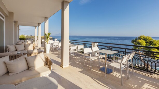 A terrace with outdoor seating, a view of the sea, and a railing.