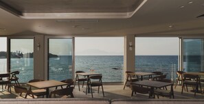 A modern dining area with large windows overlooking a body of water, featuring tables and chairs. - Alexandra Beach Resort and Spa (Zakynthos)