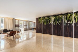 A modern lounge area with a wooden wall and hanging plants, a seating area with chairs, and a polished floor. - Alexandra Beach Resort and Spa (Zakynthos)