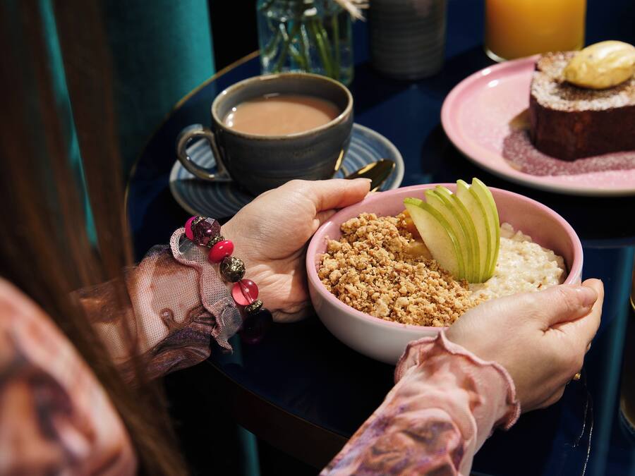 Una persona sostiene un tazón de avena con rodajas de manzana y una taza de café sobre una bandeja.