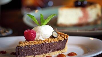 A slice of chocolate cheesecake with a raspberry and mint on a white plate.