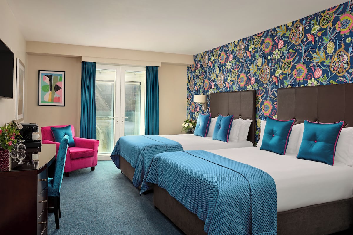 Quarto de hotel com duas camas, uma escrivaninha, uma cadeira e uma televisão.