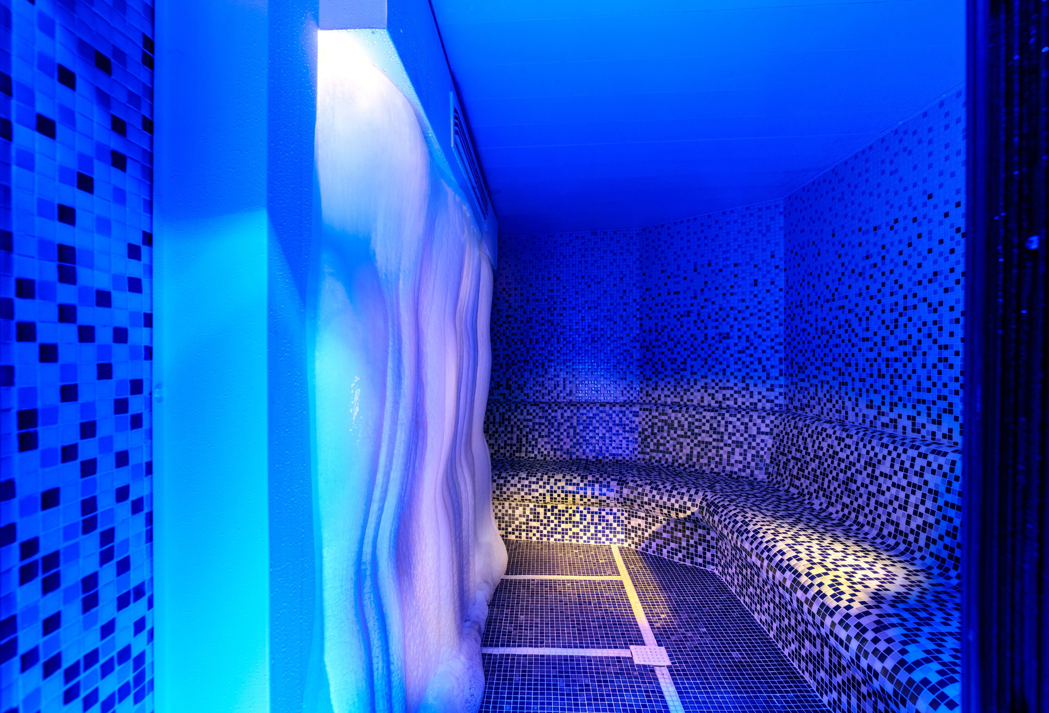 Um quarto com um piso estampado, uma cortina branca e uma parede iluminada em azul.