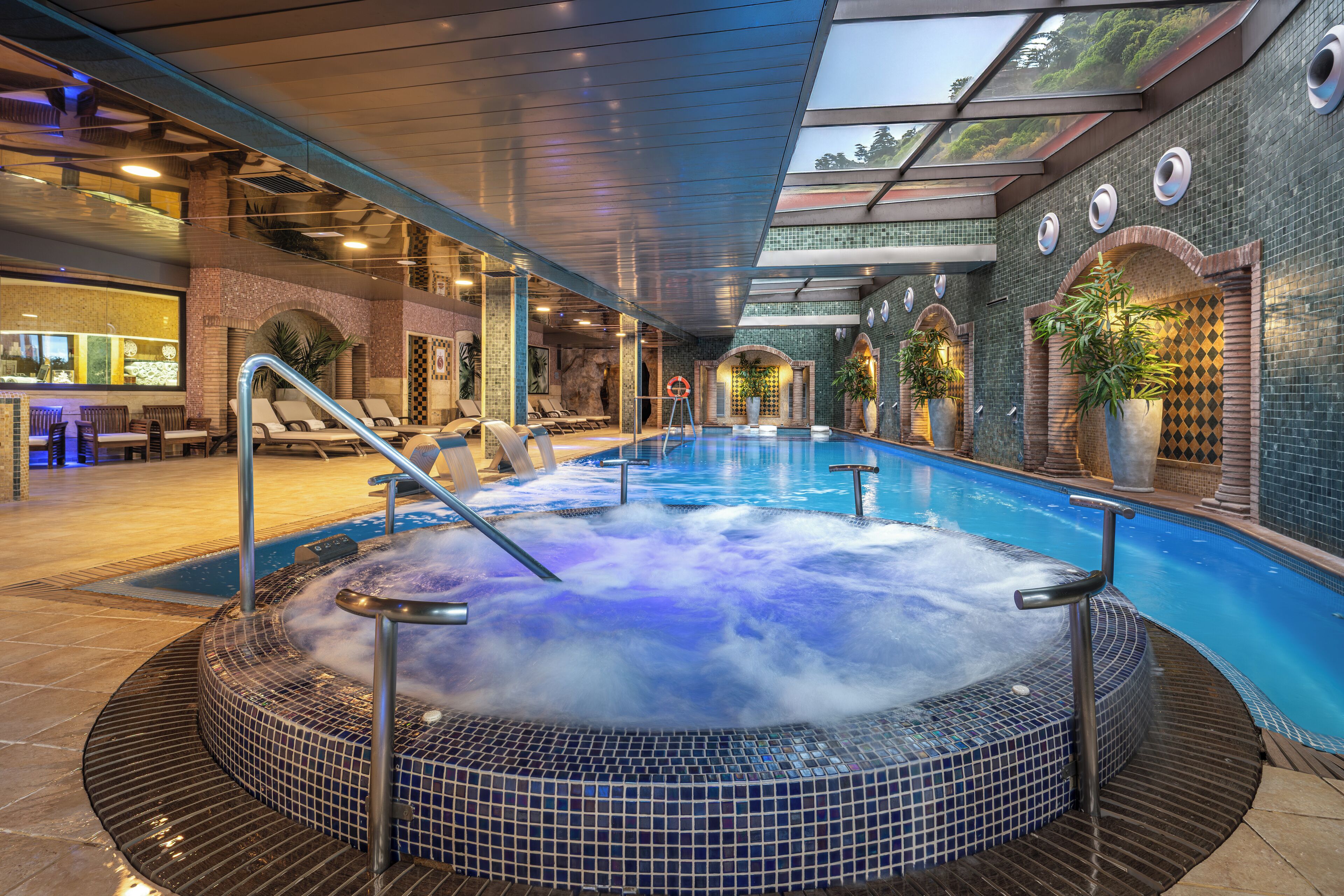 Un bain à remous avec un intérieur carrelé, entouré de chaises longues et d’une piscine.