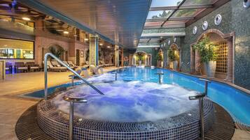 Un jacuzzi con revestimiento de azulejos, rodeado de sillones de descanso y una piscina.