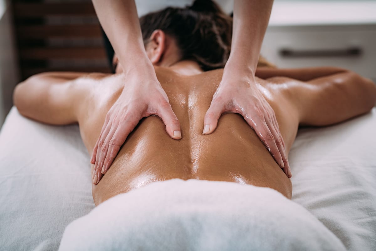Une personne reçoit un massage du dos sur un lit recouvert d'un drap blanc.