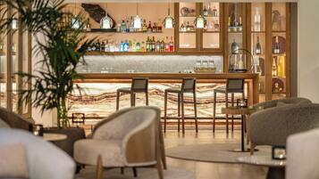 Una zona de bar con encimera de mármol, taburetes y una variedad de botellas de licor. Se observan dos sofás y una mesa de centro al frente.
