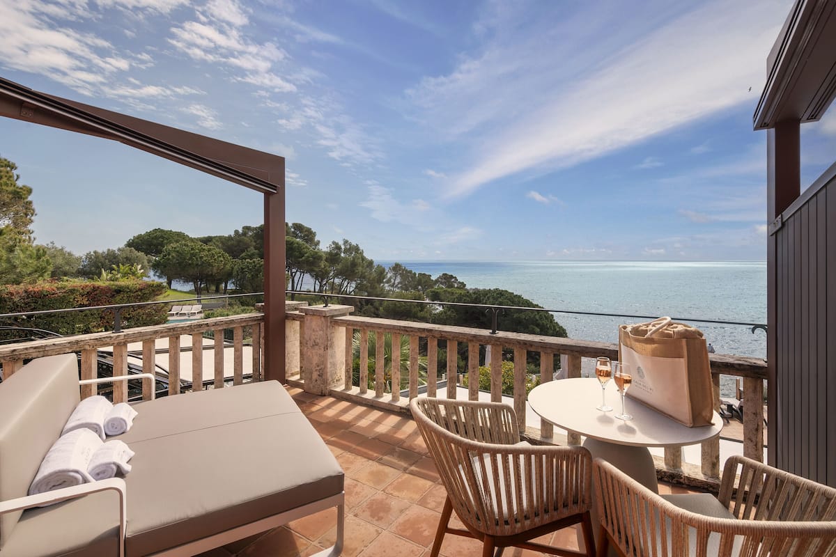 Un balcon avec vue sur la mer, une table avec un verre de vin et un sac posé sur la table.