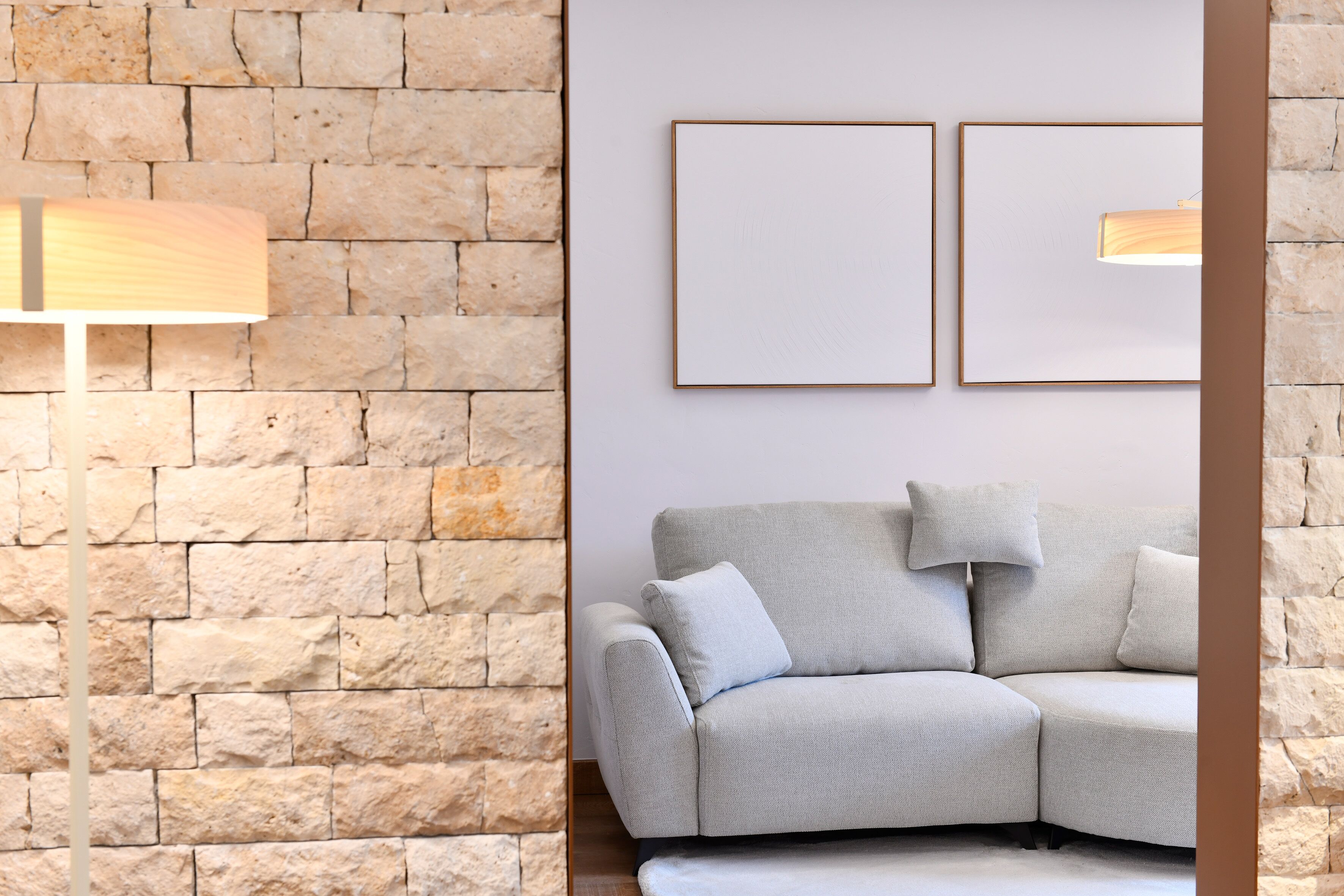 A modern living room with a stone wall, a grey sofa, and two framed pictures on the wall.