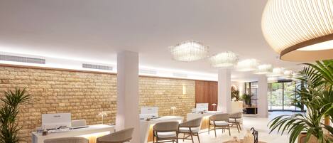 A modern hotel lobby with a stone wall, multiple computer stations, comfortable seating, and a large wooden table.