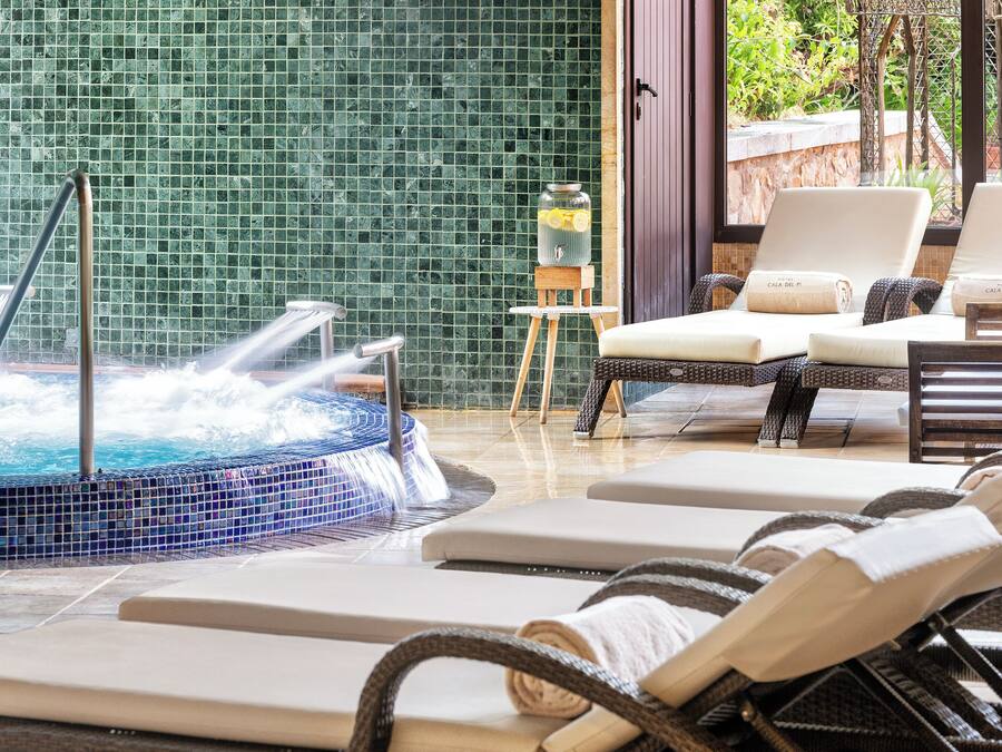 A pool area with lounge chairs, a hot tub, and a view of greenery.