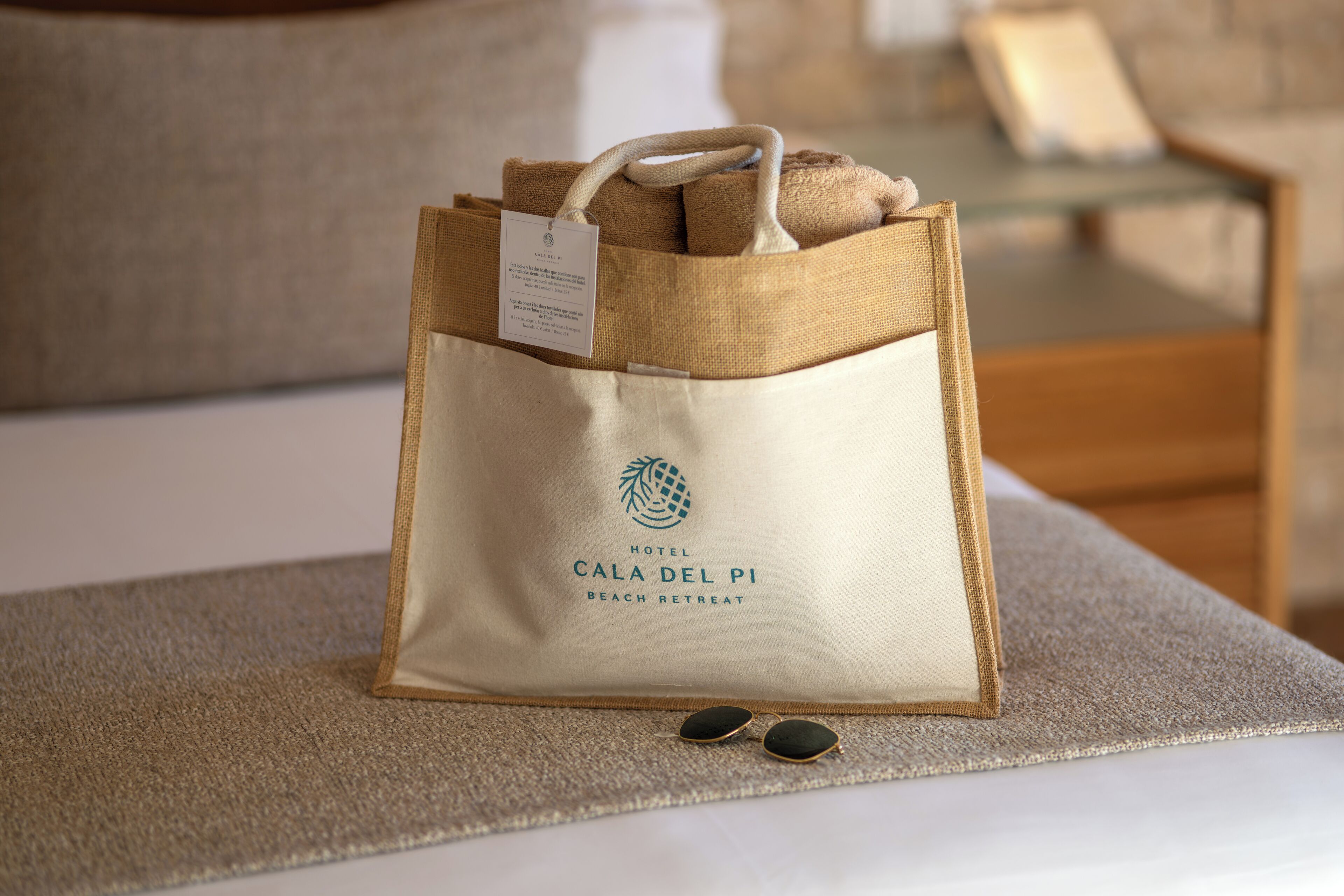 Una bossa d'hotel color beix amb una etiqueta que diu "Hotel Cala del Pi Beach Retreat" sobre un llit.