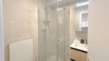 Un baño moderno con ducha envuelta en vidrio, un lavabo blanco y un espejo sobre él.