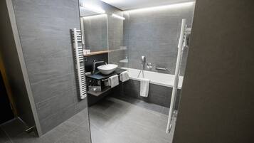 A modern bathroom with a large mirror, a white sink, a bathtub, and a shower.
