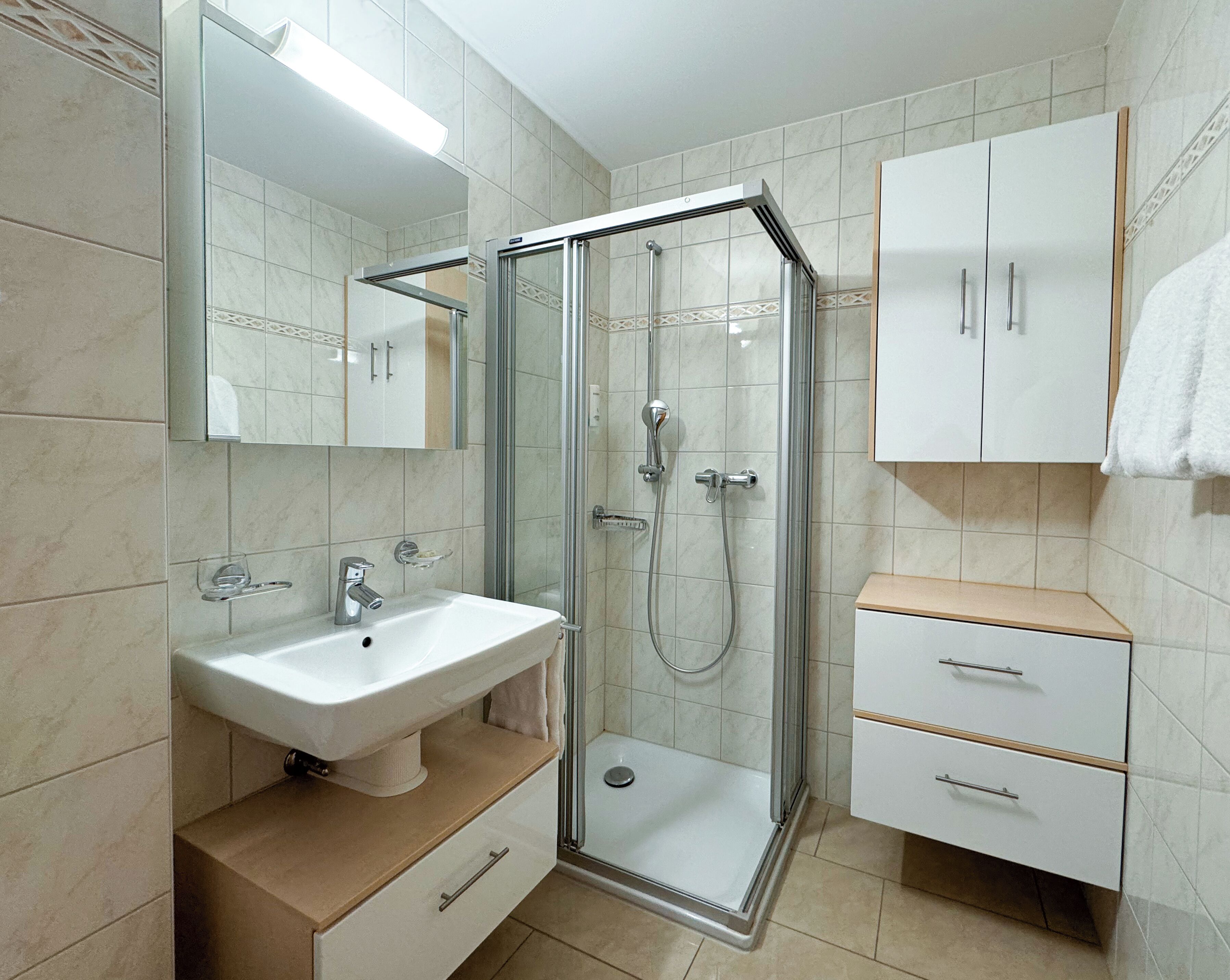 Un baño moderno con ducha de vidrio, lavamanos blanco y mueble con cajones.