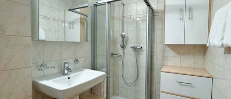 Un baño moderno con ducha de vidrio, lavamanos blanco y mueble con cajones.
